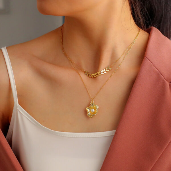 Gold-plated layered necklace with a geometric leaf chain and a shell pendant with pearl accent for a stylish and elegant look.
