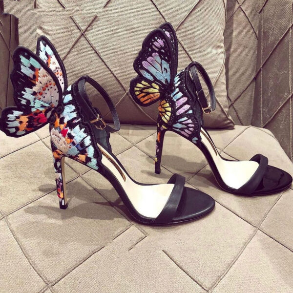 A stylish black stiletto heel sandal with a delicate butterfly wing design at the back, featuring an ankle strap and open-toe style.