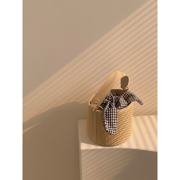 Women’s stylish bucket straw bag with a gingham fabric bow, perfect for summer fashion and casual outings.