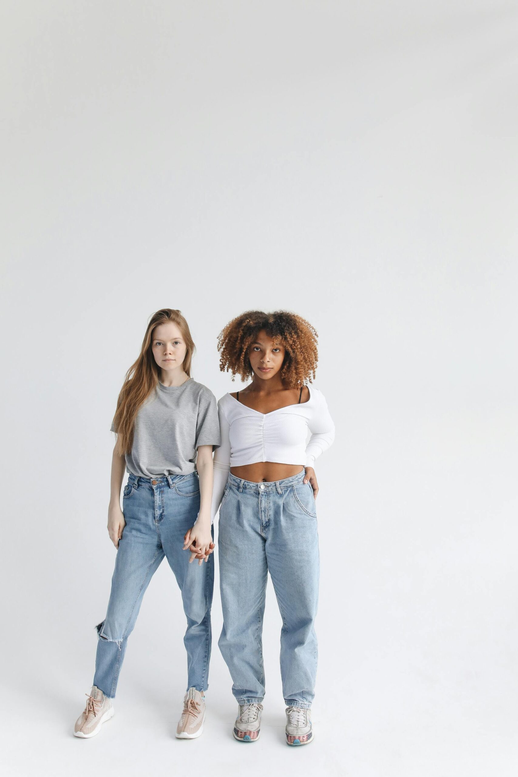 Two young women of different ethnicities standing close in a studio, symbolizing friendship and diversity.
